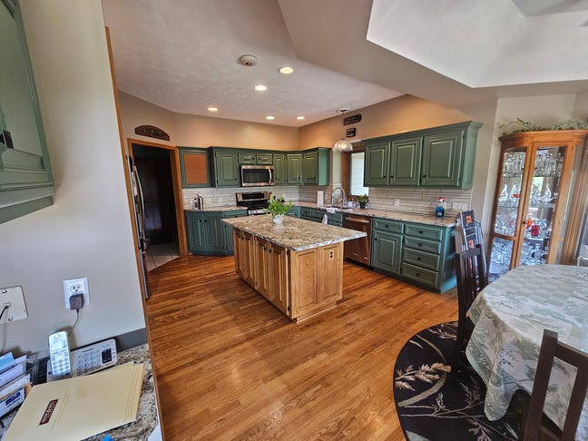 Kitchen with cabinets along the wall painted a sage green and island a natural golden oak.