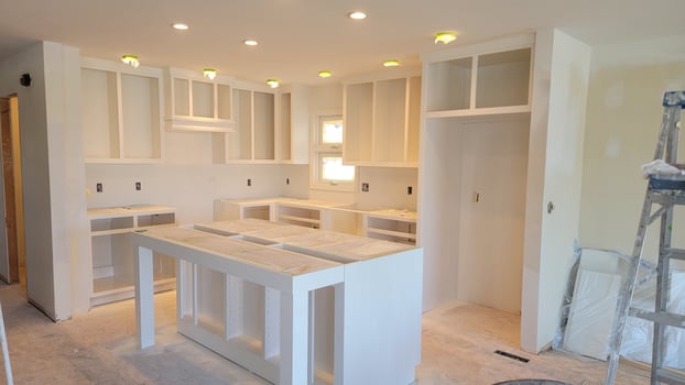 Kitchen sprayed with white paint with no countertops and cabinet doors.