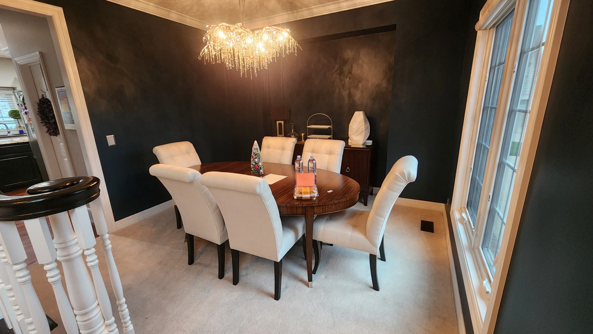 Dining room painted black with a chandelier in the center of the room with warm yellow light bulbs.