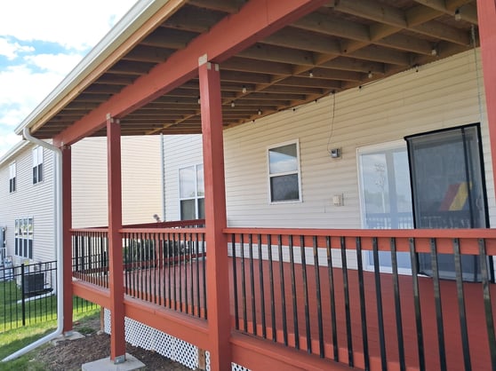 Deck on the back of a house professionally stained a deep red color with black iron bars.