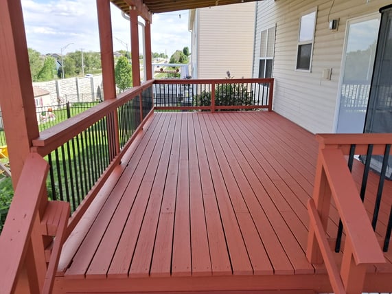 Red painted wood deck with black iron rods on the outside of a white painted home in Omaha.