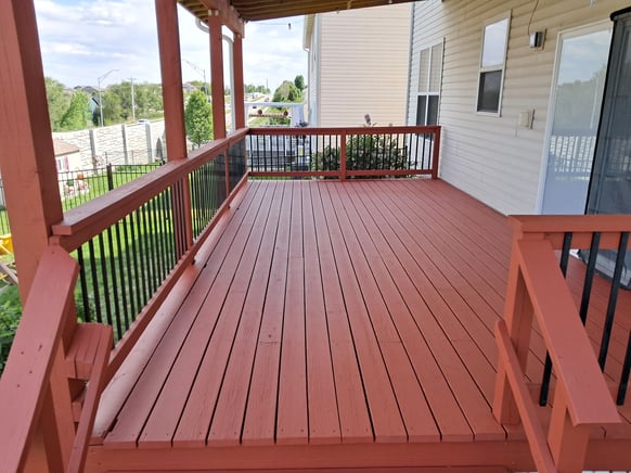 Back wood deck freshly stained with a deep red color with black iron rods.