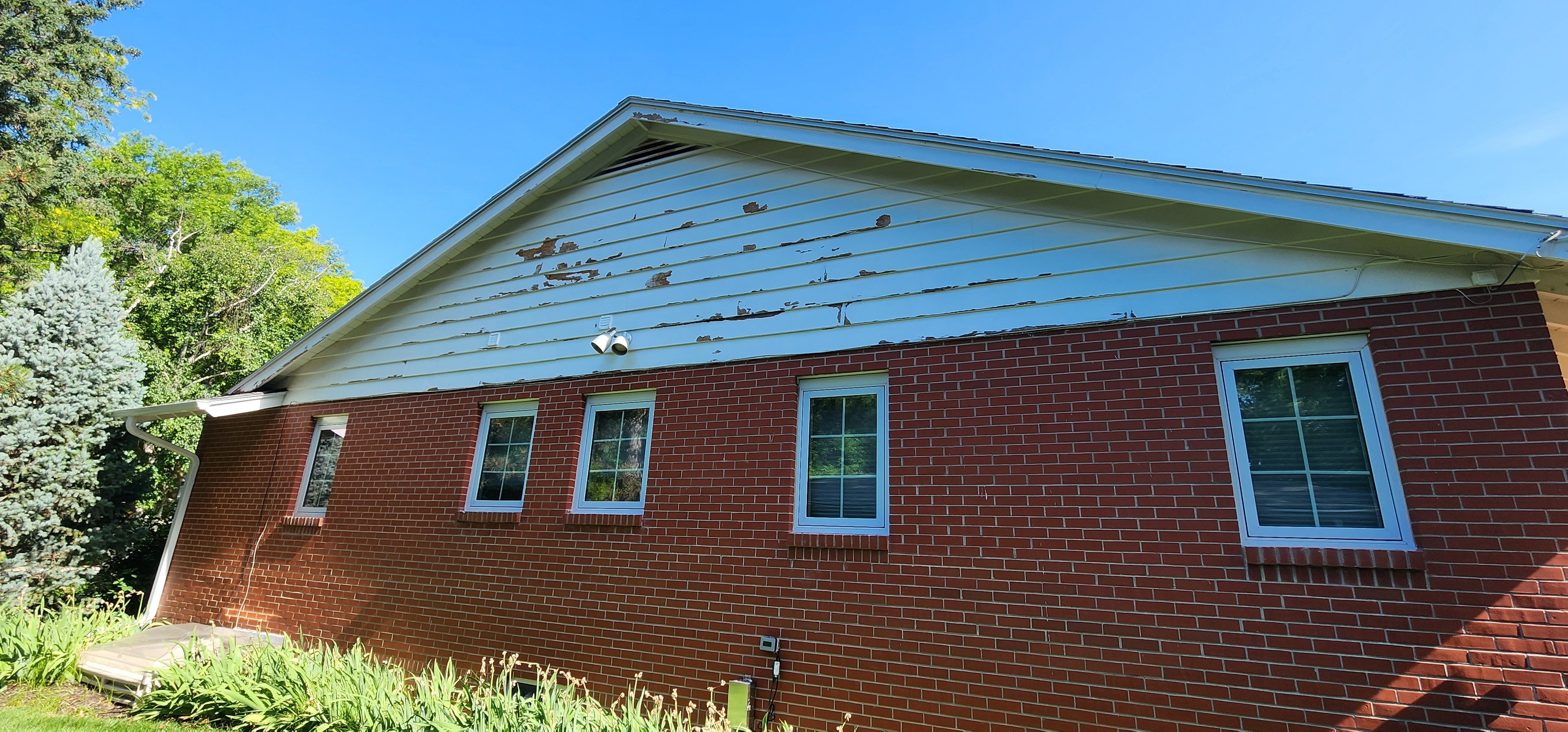 Exterior of brick house with a white painted wood siding peak with peeling paint in Omaha, NE.
