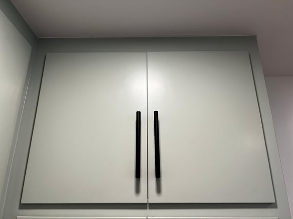Uppere cabinet doors in a home painted a light sage green color with long black handles.