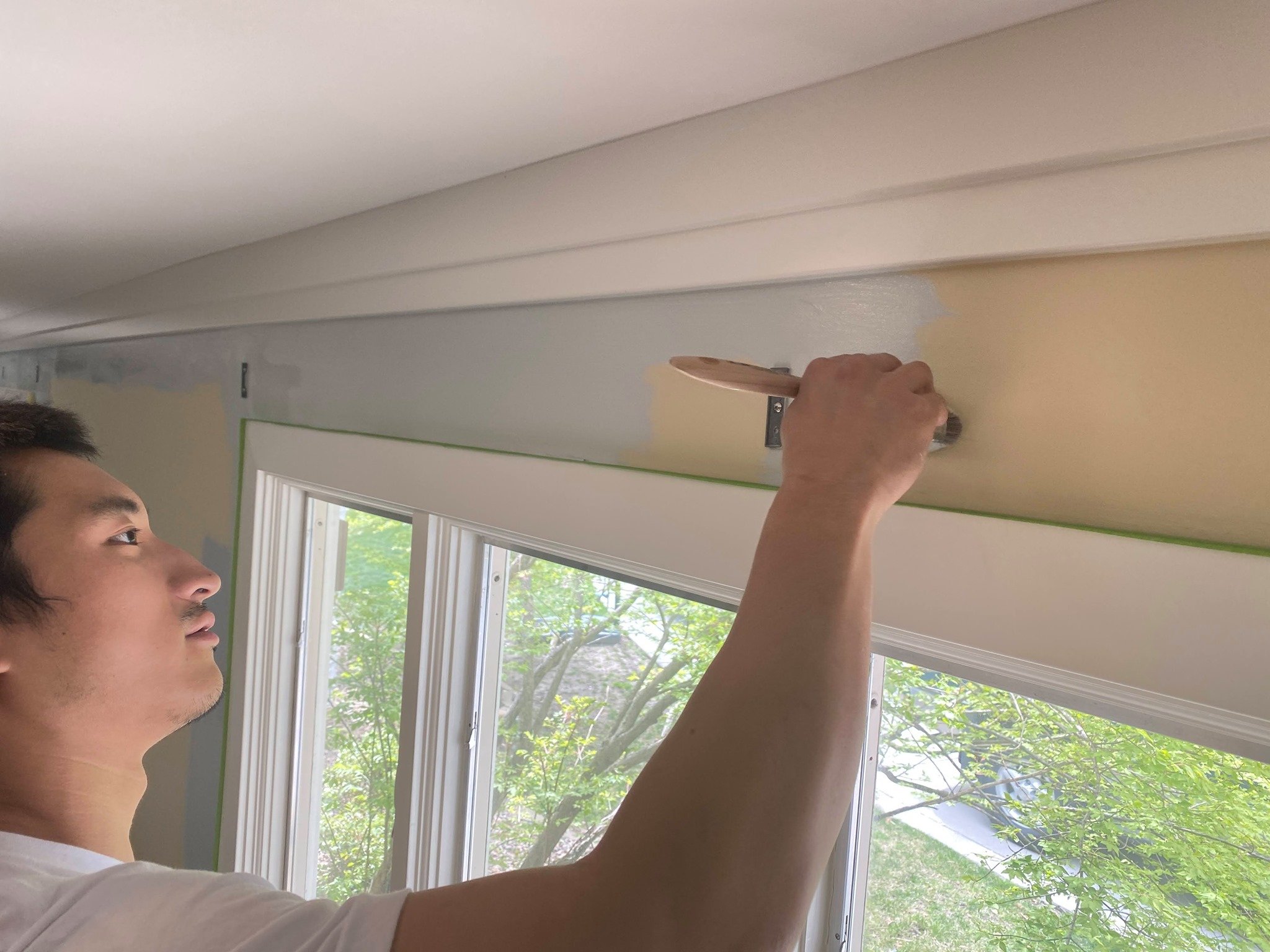 Painter brushing paint on to wall and window trim.