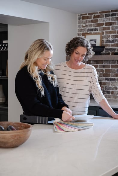 Homeowner and Leah Scheppers of Iconic Design & Styling in Omaha, NE, looking at color swatches in a kitchen on a white countertop, to choose a paint color.