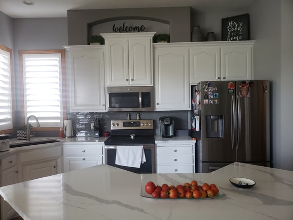 Kitchen with white cabinets painted with silver knobs and marble countertops.