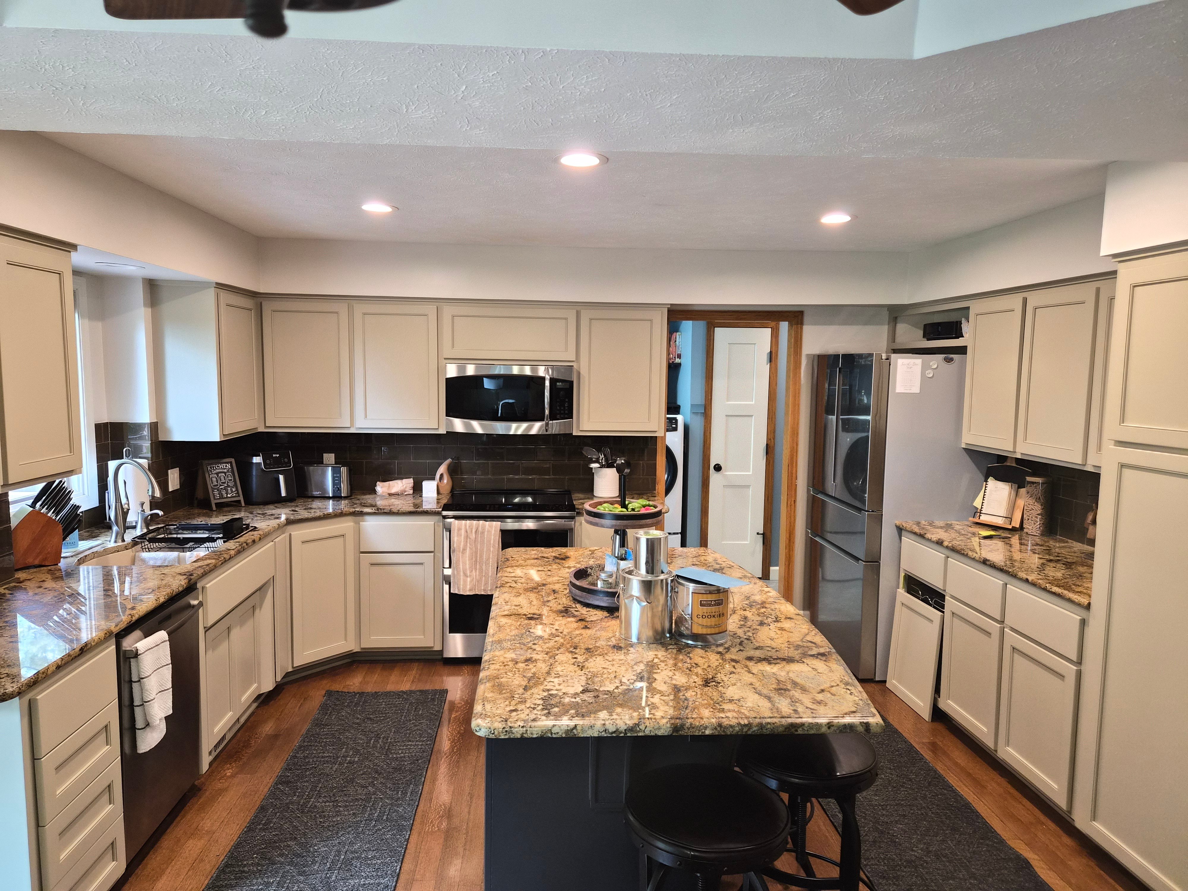 Finished painted kitchen cabinets in a beige color with a dark navy island in the center inside a home in Elkhorn, NE.