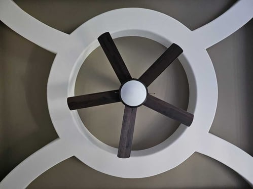 Ceiling painted beige with white wooden blocked detailing surrounding the ceiling fan.