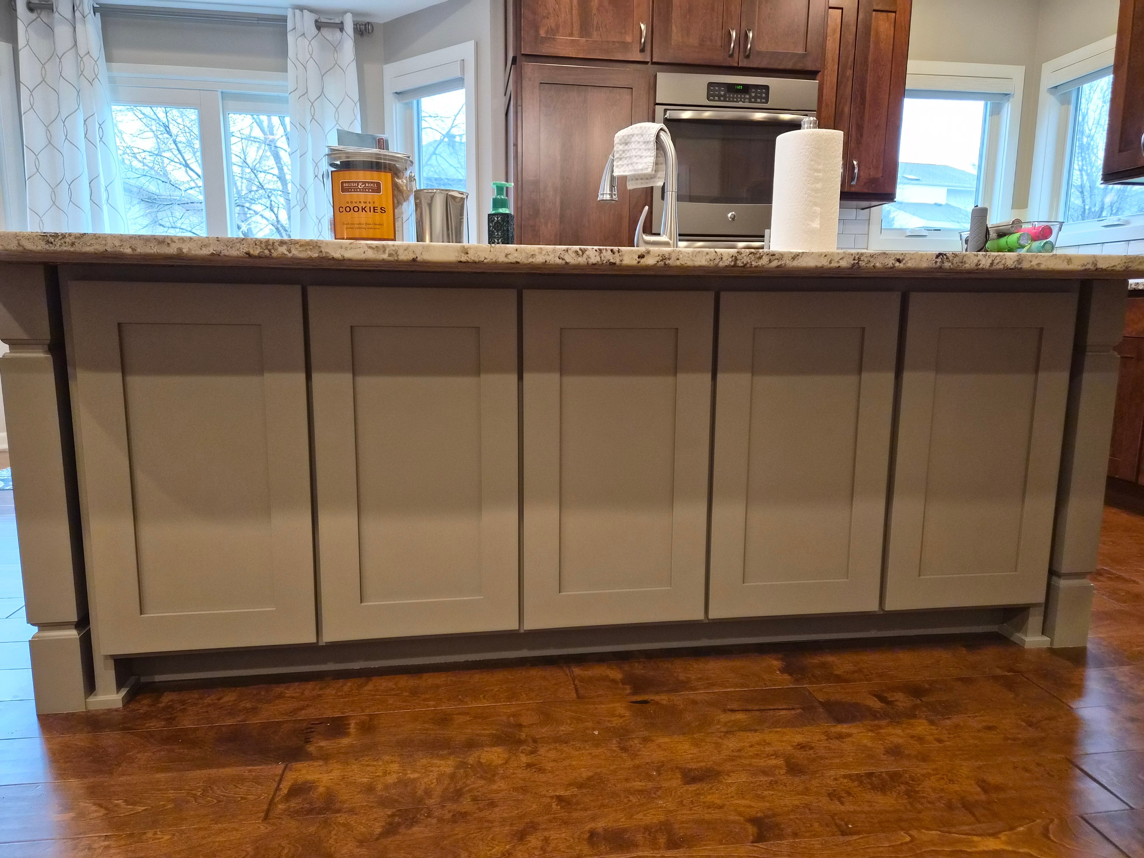 Kitchen island painted a light off white beige color with panels in the back and dark wood floors.