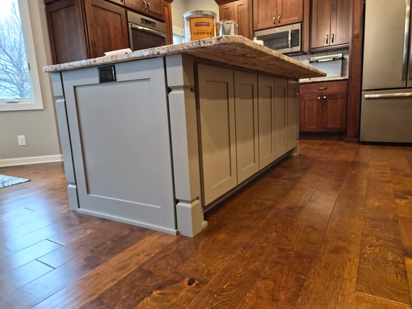 Finished painted kitchen island a greige color with stained cabinets along the walls.