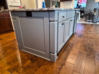 Side of kitchen cabinet island painted a greige color with a outlet on the side.