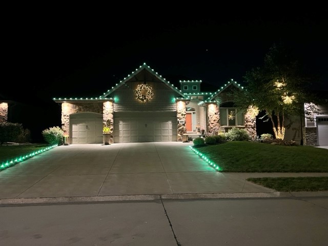 Christmas lights installed on a roofline and along a driveway with a wreath above the garage outside of a home in Omaha, NE.