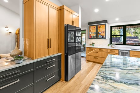 Kitchen with new cabinets with natural warm wood and dark painted cabinets with long silver and black handles in a modern kitchen.