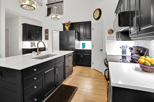Cabinets painted black in a kitchen with white countertops, walls, and backsplash.
