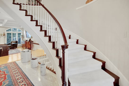 Close up of railing and banister painted white and stairs and railing stained a dark brown with a runner on the stairs and a white wall.