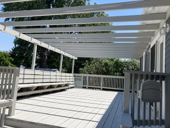 Wooden deck painted white with a built in seating bench and a pergola on top.