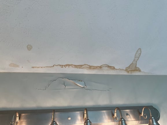 Water stain on white painted ceiling and wall damage inside a bathroom in a Omaha home.
