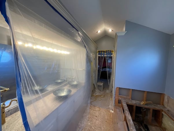 Bathroom in the process of being painted with a large plastic tarp covering the sinks and vanity.