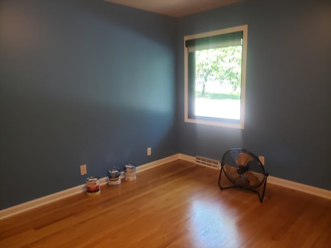 Bedroom painted a bright blue with warm wood floors and white trim.