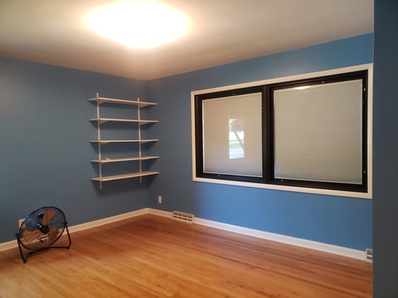 Bedroom painted a darker blue color with white trim around the window and the baseboards.
