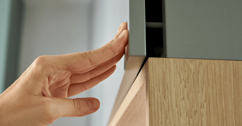 Persons hand touching corner of sage green cabinet door.