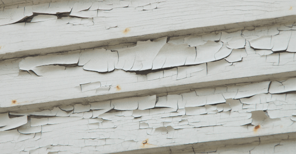 Exterior siding on house with very damaged, peeling white paint.
