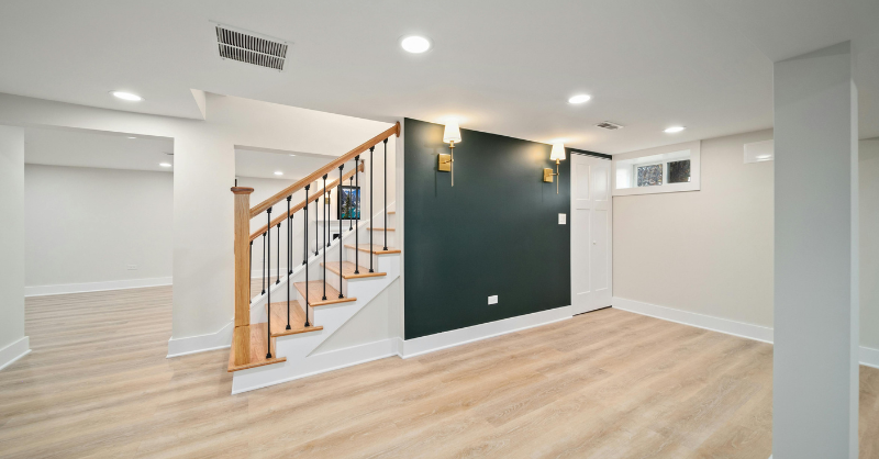 Basement with warm off white walls, a black accent wall, bright white baseboards, and light wood floors in a new build home in Omaha, NE.