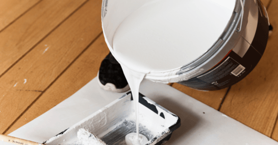 White paint primer in a large bucket being poured into a paint tray before it is painted on interior walls. 