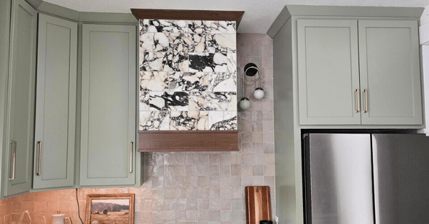 Kitchen with light green cabinets and marble oven vent with brown stained trim,