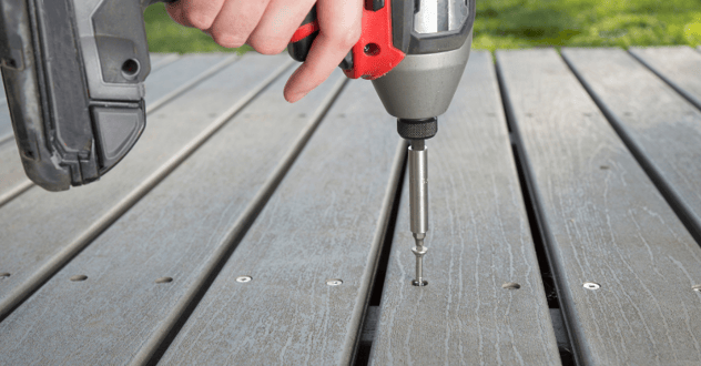 Person screwing screw with a drill into a deck board to repair it.