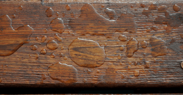 water puddles on wooden deck board stained a dark brown.