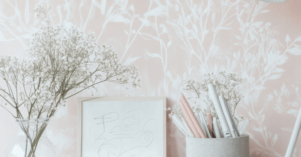 Pink wallpaper with branches against a wall with decor on a table.