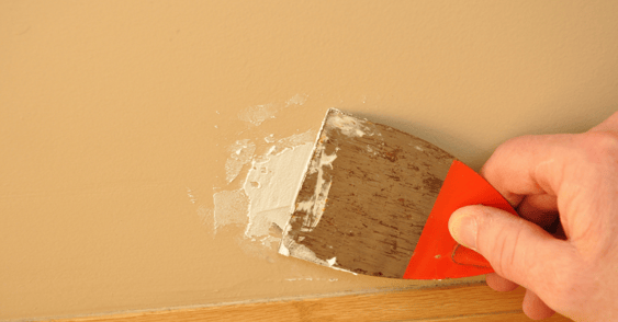 Person using a scraper to apply spackle to a beige colored wall in Omaha.
