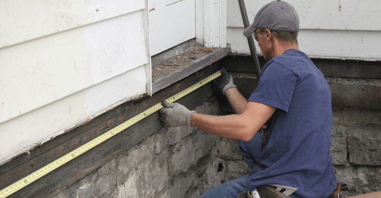 Contractor measuring exterior of home with measuring tape before painting.