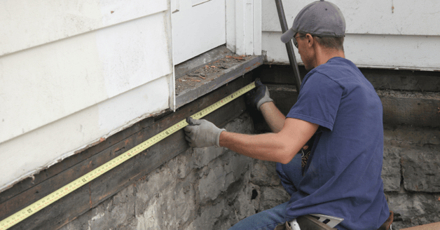 Man measuring exterior trim of a house that needs painted.
