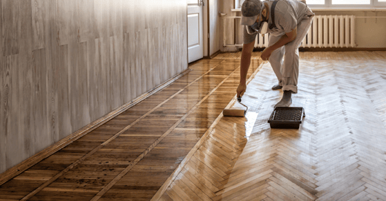 Painter rolling stain on wooden floor.