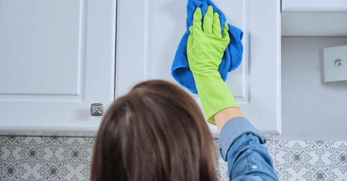 Woman wiping kitchen cabinets that were painted white with a cloth.