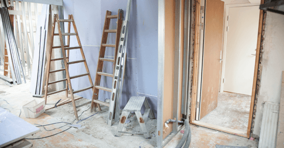 Interior of house in construction with ladders against the wall while painting ceiling of room.