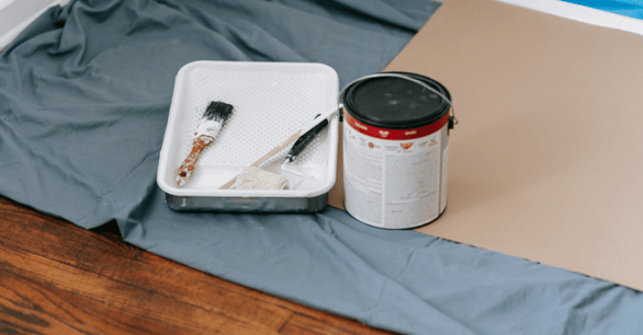 Paint can, trey and brushes laid on the floor of a interior room with a drop cloth.