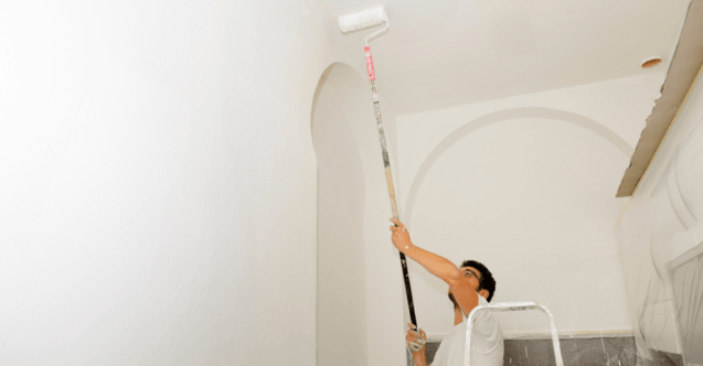 Painter rolling white paint onto a ceiling with a extender.