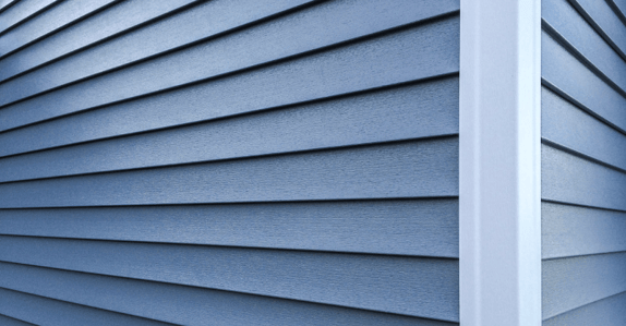 Corner of house with dark blue vinyl siding and white trim.