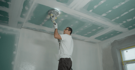 Contractor fixing light fixture to paint ceiling white.