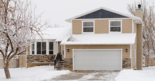 Exterior of house in Omaha in show in yard and on the roof. The house is painted a light yellow with stone along the bottom and white trim and garage doors.