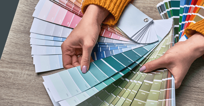 Persons hand holding out blue and green color swatches on a table.