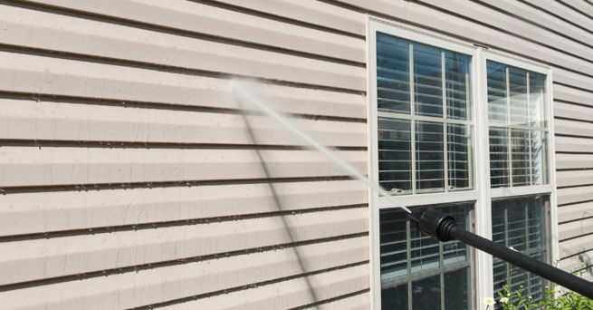 Pressure washer hitting beige exterior siding of a house in Omaha, NE.