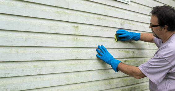 Dirty exterior of a home with a man with a sponge cleaning the light green siding.