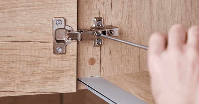Screw being tightened on a cabinet door hinge.