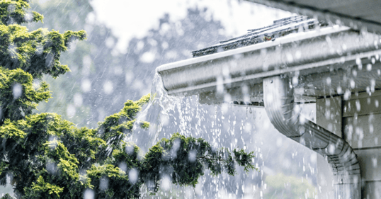 Corner of house in the rain with water dripping off the roof.