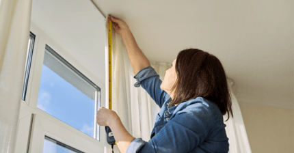 Woman measuring window with tape measure.